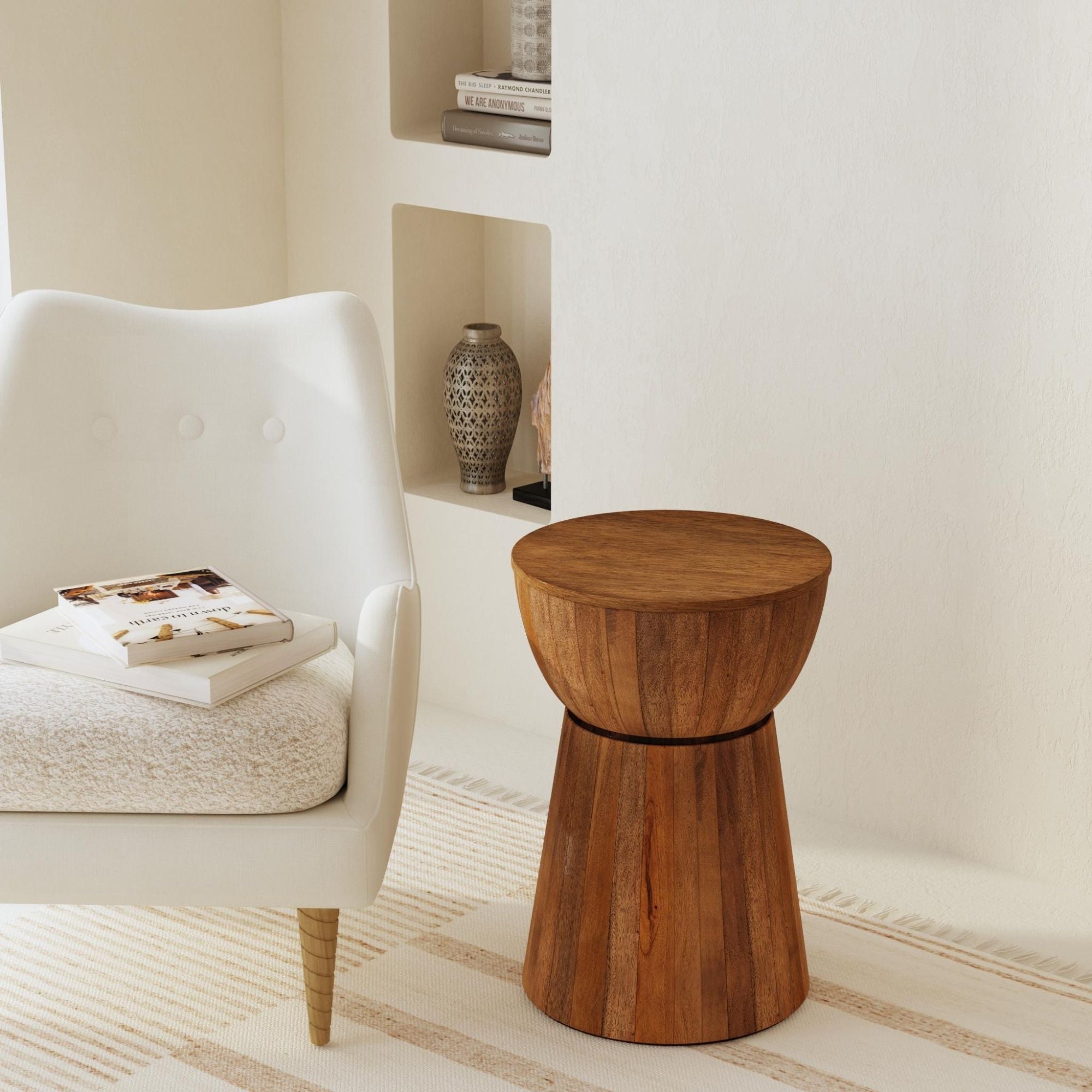 Light wood-toned drum side table next to a beige sofa, on a patterned rug, with books and coffee cup on top.